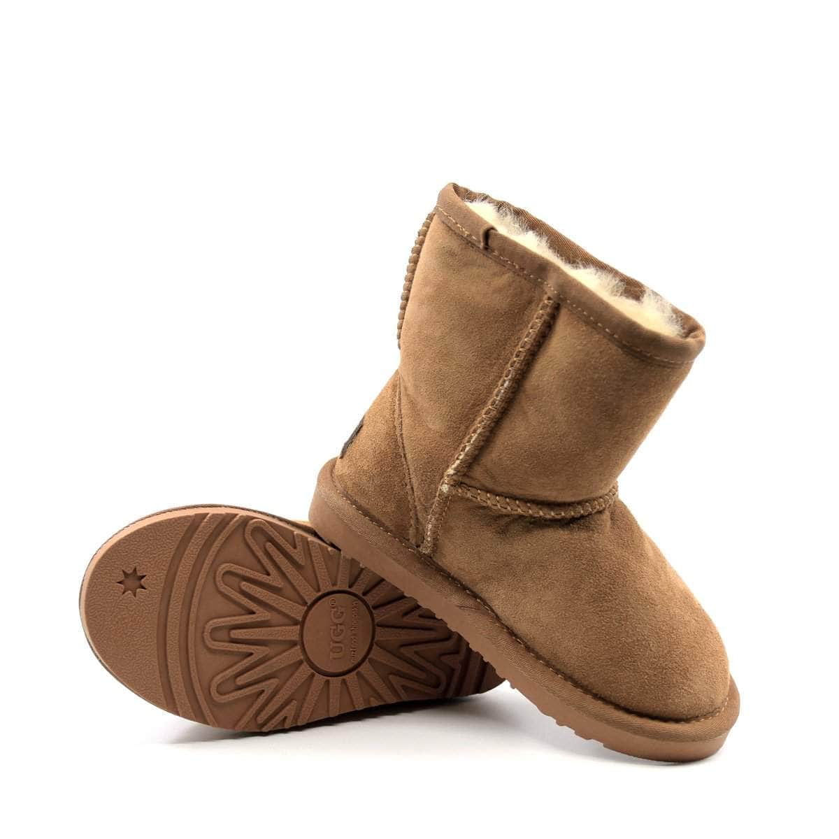 A pair of UGG Kids Short Classic Boots in tan, featuring plush sheepskin lining and suede exterior, designed for children.